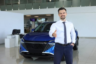 Yeni mavi arabanın yanında müşteriyle tokalaşmaya çalışan mutlu bir satıcı.