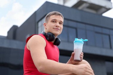Protein salgılayan atletik bir adam açık havada içiyor, düşük açılı.
