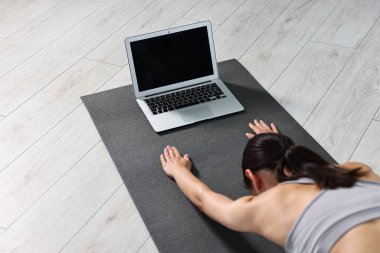 Evde laptopun yanında yoga yapan bir kadın.