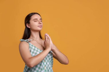 İyi bir sınav için dua eden genç öğrenci turuncu arka planda, metin için boşluk bırakıyor