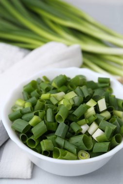 Kavanozda doğranmış yeşil soğan ve sapları beyaz masada, yakın plan.