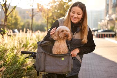 Bisikletli ve sevimli oyuncak köpekli bir kadın güneşli bir günde evcil hayvan taşıyıcısında.