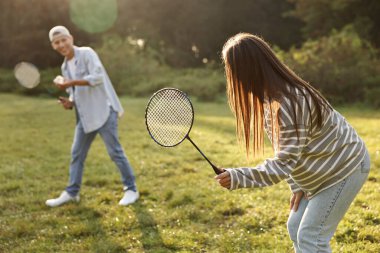 Genç adam ve kadın güneşli bir günde parkta badminton oynuyorlar.