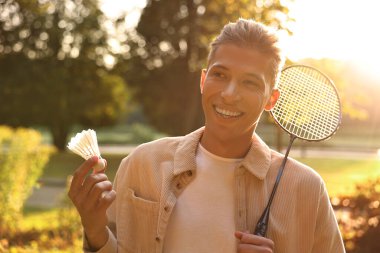 Güneşli bir günde parkta badminton raketi ve pipisi olan mutlu genç bir adam.