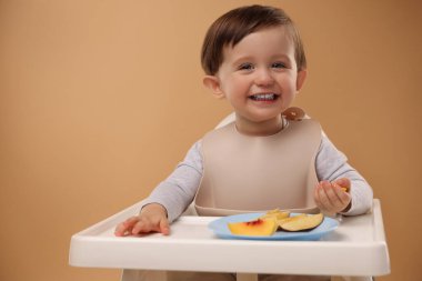 Sağlıklı bebek maması. Sevimli küçük çocuk bej arka planda yüksek sandalyede meyve yiyor, mesaj atmak için yer var.