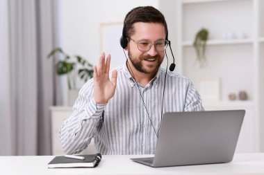 İçerideki beyaz masada dizüstü bilgisayarla görüntülü konuşma yapan kulaklık çevirmeni