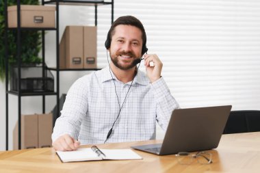 Interpreter in headset having video chat via laptop at wooden table indoors clipart