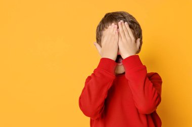 Korkak küçük çocuk turuncu arka planda yüzünü kapatıyor. Metin için boşluk