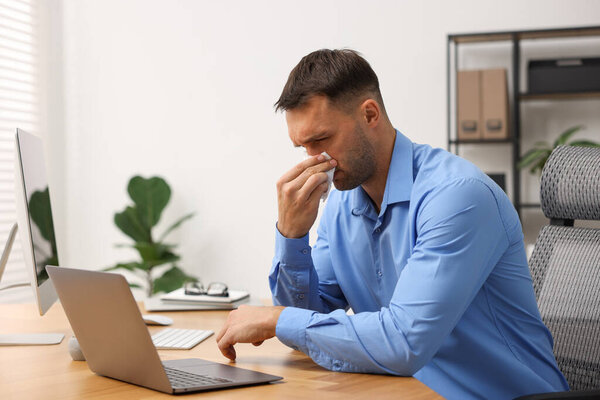 Sick man with runny nose at table in office