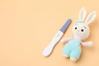 Hamilelik testi ve soluk turuncu arka planda oyuncak tavşan, mesaj için boşluk