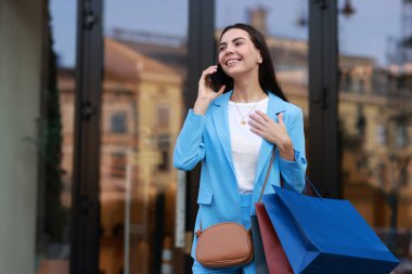 Renkli alışveriş çantalı mutlu kadın dışarıda akıllı telefondan konuşuyor, mesaj atmak için yer var.