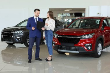 Satıcı ve müşteri salonda yeni kırmızı arabanın yanında.