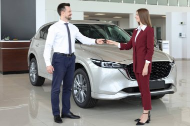 Satıcı, salonda yeni bir arabanın yakınındaki müşteriye anahtarı veriyor.