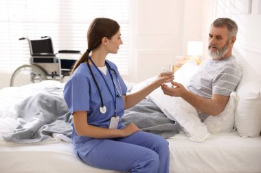 Bakıcı, yatağın içindeki yaşlı adama su veriyor. Ev sağlık hizmetleri