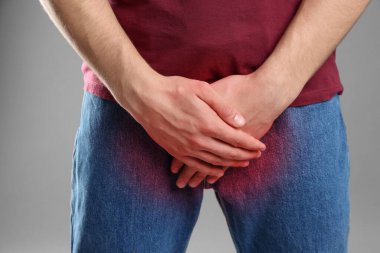 Cinsel yolla bulaşan hastalıklar. Gri arka planda kasıklarına yakın el ele tutuşan adam, yakın plan.