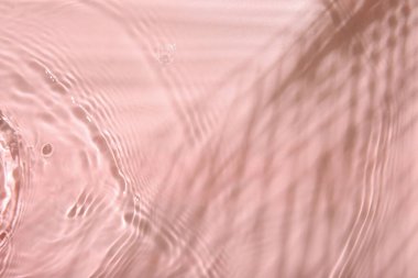 Pembe arka planda dalgalı berrak su yüzeyi, üst görünüm