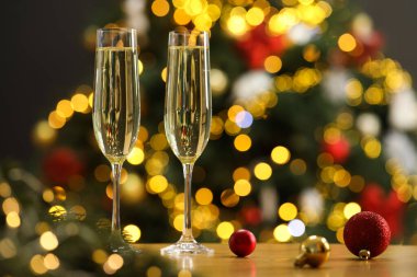 Şampanya bardaklar içinde ve ahşap masada bulanık Noel ışıklarına karşı şenlikli süsler, yazı için yer. Bokeh etkisi
