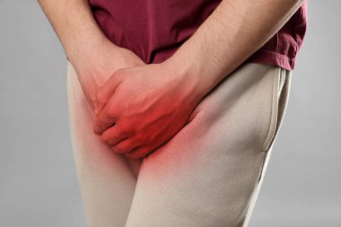 Cinsel yolla bulaşan hastalıklar. Gri arka planda kasıklarına yakın el ele tutuşan adam, yakın plan.