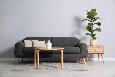 Rahat bir kanepe, çiçek ve gri duvarın yanındaki masalar.