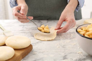 Woman making pirozhki (stuffed pastry pies) with apples at white marble table, closeup clipart