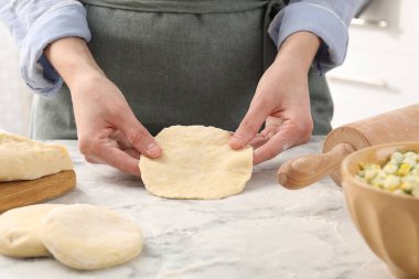 Beyaz mermer masada pirozhki yapan bir kadın, yakın plan.