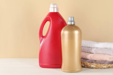 Çamaşır deterjanı dolu şişeler ve beyaz ahşap masa üzerinde bej arka planda temiz havlular.