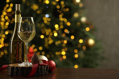 Bulanık ışıklara karşı ahşap masanın üzerinde Noel dekoru olan cam ve bir şişe beyaz şarap, mesaj için yer. Bokeh etkisi