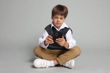 Gri arka planda akıllı telefonu olan şirin bir çocuk.