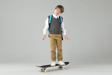 Açık gri arka planda kaykayı olan küçük bir çocuk.