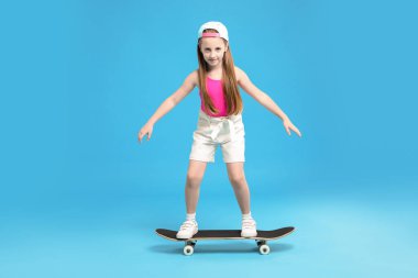 Açık mavi arka planda kaykayın üzerinde duran küçük kız