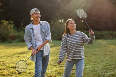 Genç kadın ve adam güneşli bir günde parkta badminton oynuyorlar.