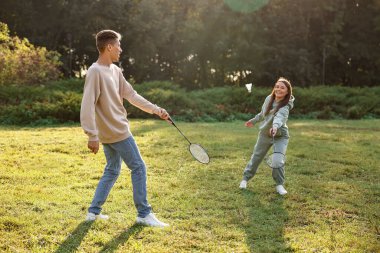 Güneşli bir günde parkta badminton oynayan genç bir kadın ve erkek.