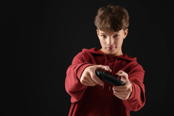 Teenage boy playing video game with controller on black background. Space for text