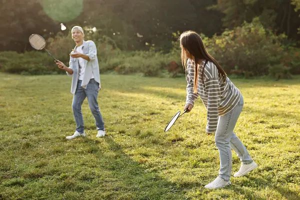 Genç adam ve kadın güneşli bir günde parkta badminton oynuyorlar.