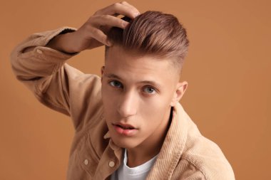 Kahverengi arka planda şık saç kesimi olan kendine güvenen genç bir adam.