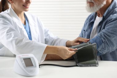 Hastanedeki randevu sırasında yaşlı adamın kan basıncını ölçen doktor, yakın plan.