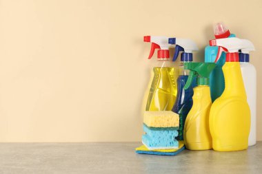 Gri masadaki farklı temizlik ürünleri ve malzemeler bej arka planda, metin için yer