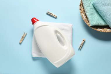 Çamaşır deterjanı şişesi, temiz havlular ve açık mavi arka planda mandallar.