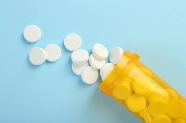 Açık mavi arka planda bir şişe antibiyotik hapı.