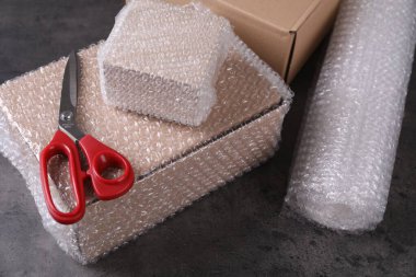 Cardboard boxes, bubble wrap and scissors on dark grey table