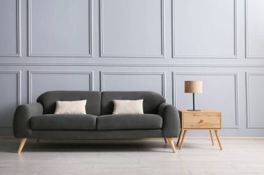 Gri duvarın yanındaki sehpada yastıklı ve lambalı şık bir kanepe.