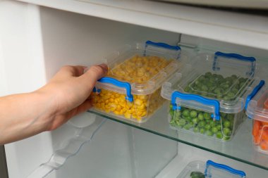 Buzdolabından dondurulmuş mısırlı plastik kap alan kadın, yakın plan.