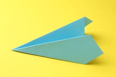 Sarı arka planda bir el yapımı açık mavi kağıt uçak.