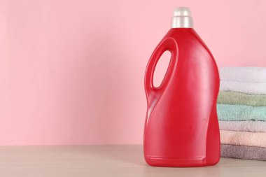 Çamaşır deterjanı şişesi ve ahşap masa üzerinde temiz havlular pembe arka planda, mesaj için yer