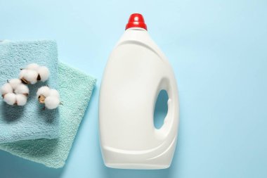 Çamaşır deterjanı şişesi, temiz havlular ve açık mavi arka planda pamuk çiçekleri.