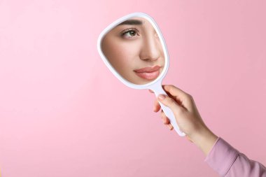 Güzel bir kadın pembe arka planda el yapımı aynaya bakıyor, yakın plan.