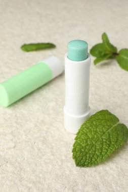 Mint lip balms and green leaves on beige textured table, closeup. Cosmetic product clipart