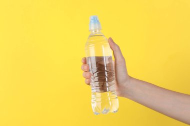 Sarı arka planda plastik su şişesi tutan kadın, yakın plan. Metin için boşluk