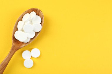 Sarı arka planda kaşıkta antibiyotik haplar, üst manzara. Metin için boşluk