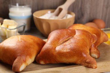 Lezzetli pirozhki (dolgulu börek) ve ahşap masa üzerindeki malzemeler, yakın plan.